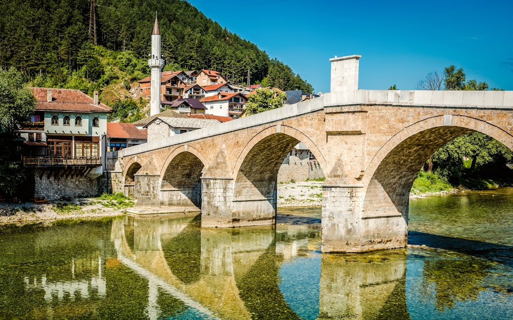 Old stone bridge over Neretva River in Konjic, Bosnia and Herzegovina with nearby houses.