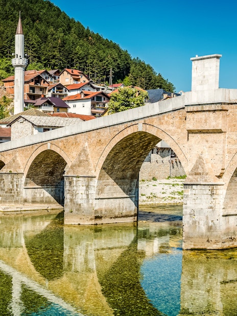 Old stone bridge over Neretva River in Konjic, Bosnia and Herzegovina with nearby houses.