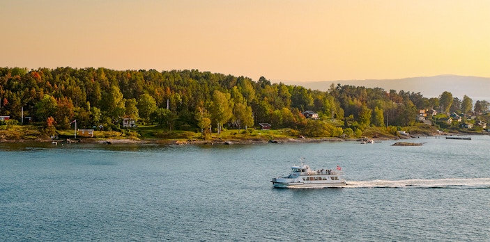 Cruise boat on Oslo Fjord with autumn foliage in the background.