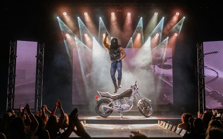 Performer jumping on stage with motorcycle during Chippendales act.