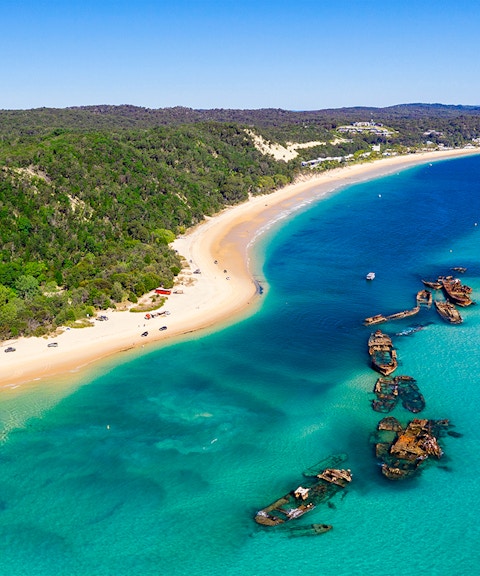 Shipwrecks along the coast of Moreton Island with clear blue waters and sandy beach.