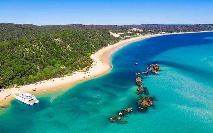 Shipwrecks along the coast of Moreton Island with clear blue waters and sandy beach.