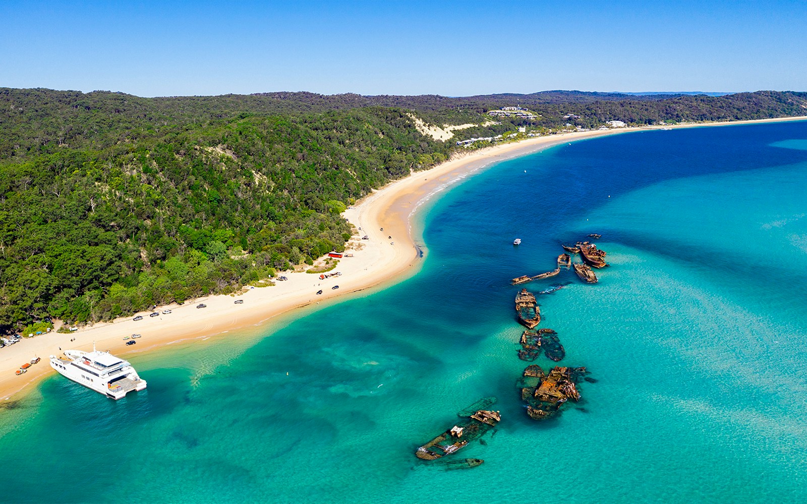 Shipwrecks along the coast of Moreton Island with clear blue waters and sandy beach.
