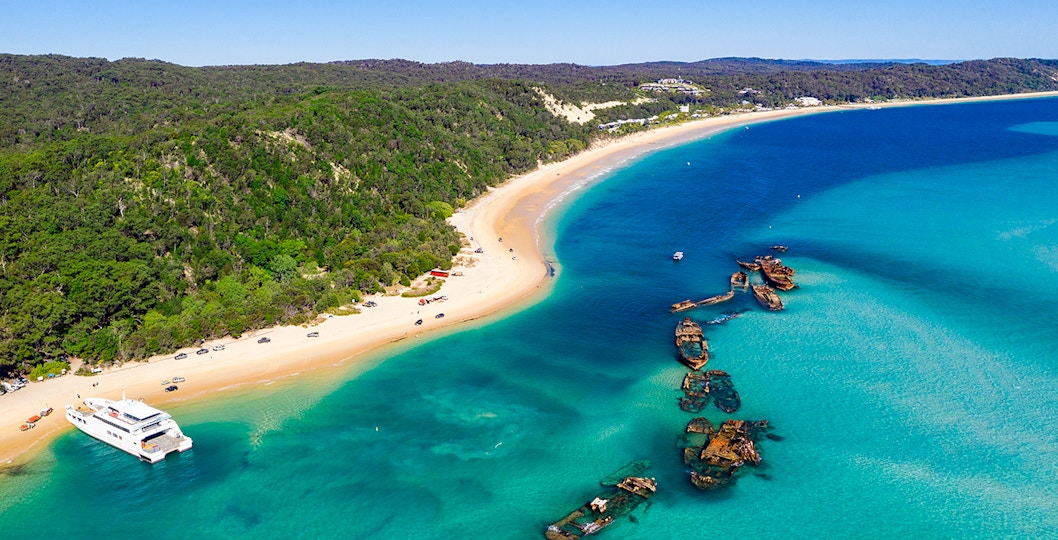 Shipwrecks along the coast of Moreton Island with clear blue waters and sandy beach.