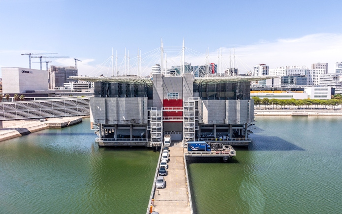 Lisbon Oceanarium building surrounded by water with cityscape in the background.