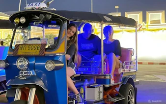 Tuk tuk with passengers on a Bangkok street at night.