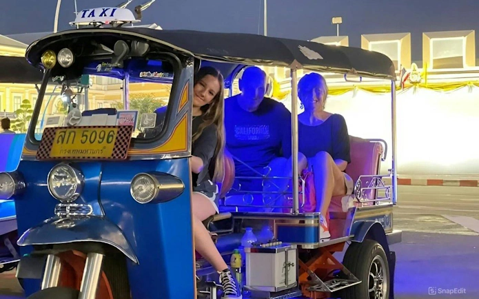 Tuk tuk with passengers on a Bangkok street at night.