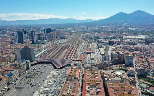 Aerial view of Naples central railway station and surrounding cityscape with Mount Vesuvius in the background.