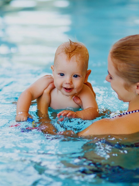 Baby swimming with adult in a pool.