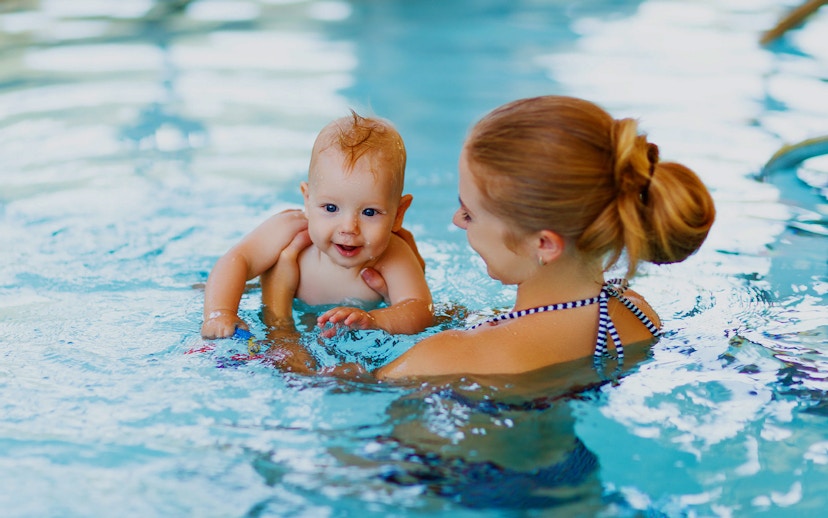 Baby swimming with adult in a pool.