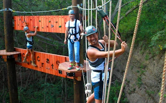 Participants navigating high-elevation ropes course with safety gear in forest setting.