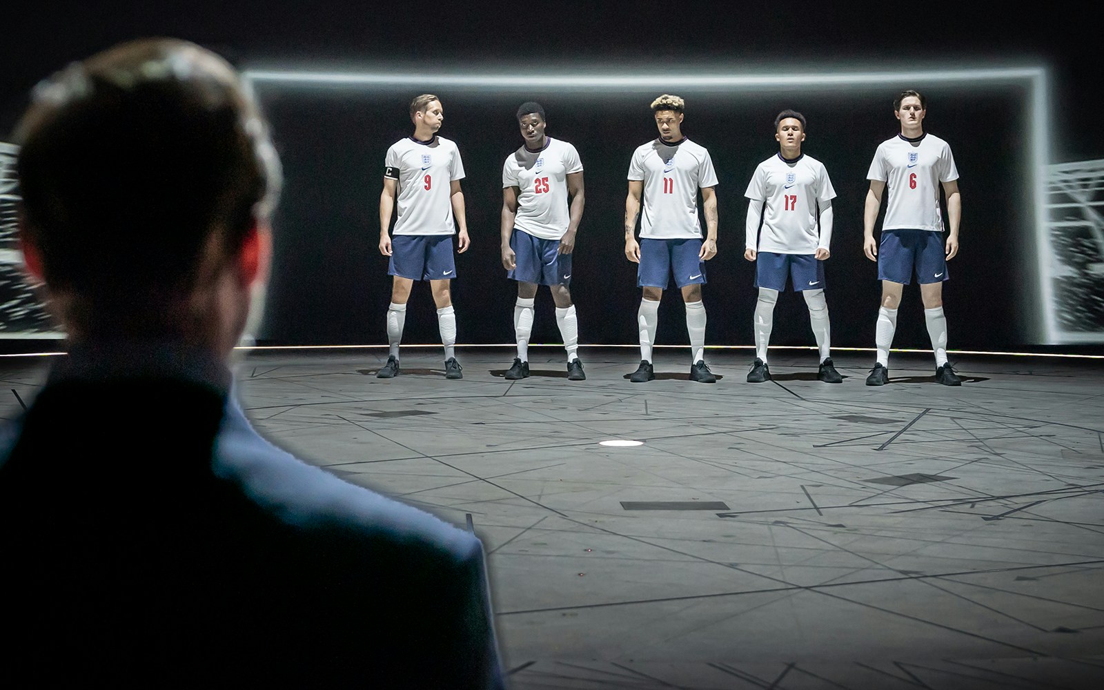 Five soccer players in England jerseys stand on stage facing an audience, related to "Dear England.