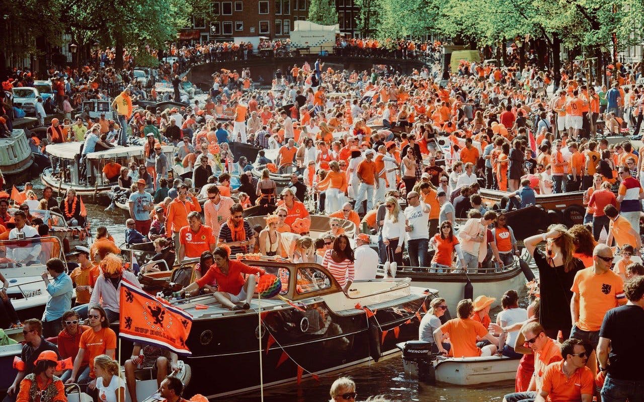 Crowds in orange celebrate on boats during Amsterdam Kingsday party cruise.