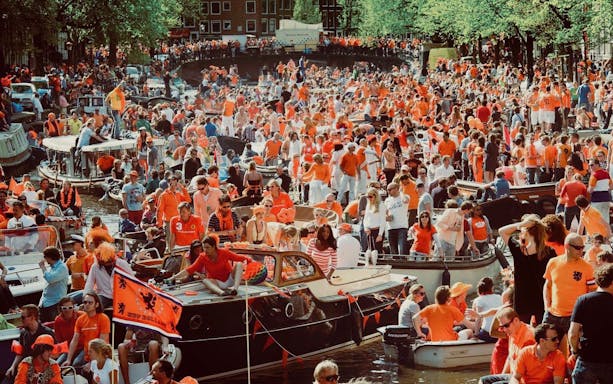 Crowds in orange celebrate on boats during Amsterdam Kingsday party cruise.
