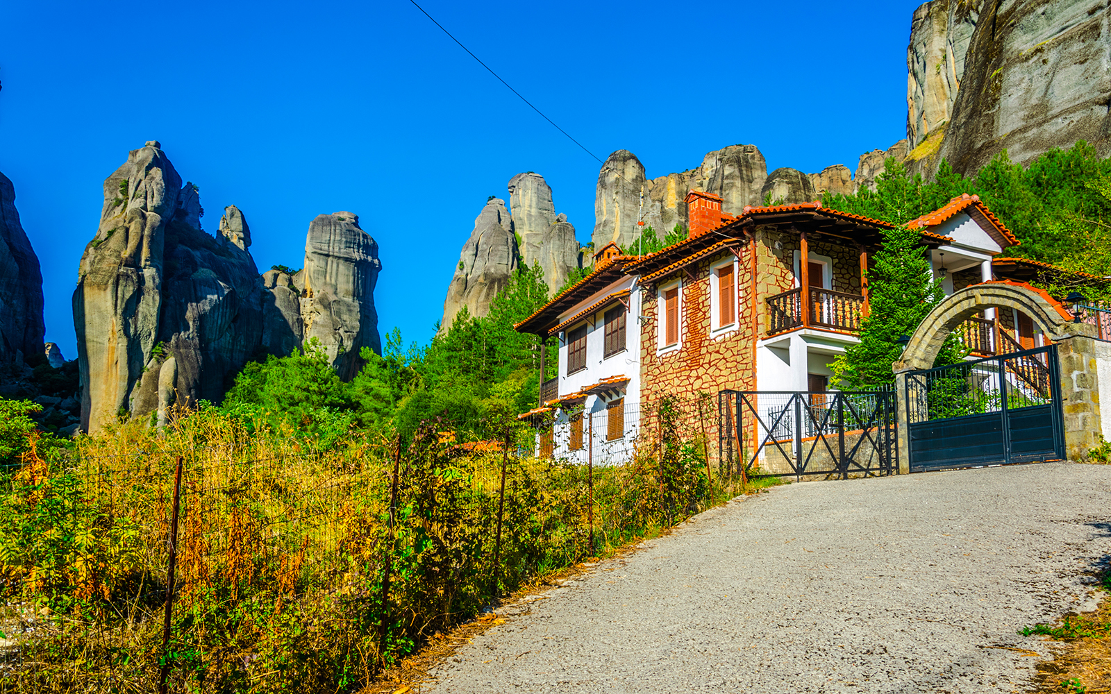 House with stone facade and red roof in Kastraki village, Greece, with Meteora rock formations in the background.