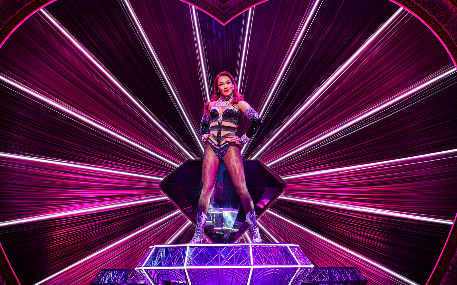 Performer on stage at Moulin Rouge! The Musical, West End, with vibrant pink lighting.