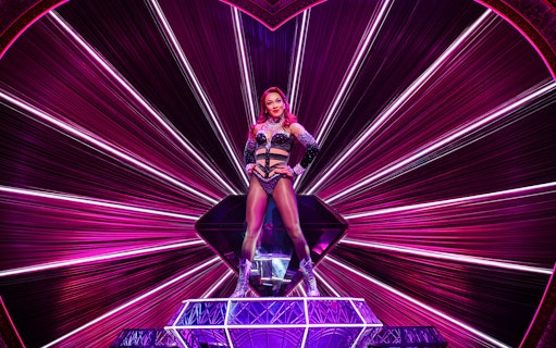Performer on stage at Moulin Rouge! The Musical, West End, with vibrant pink lighting.