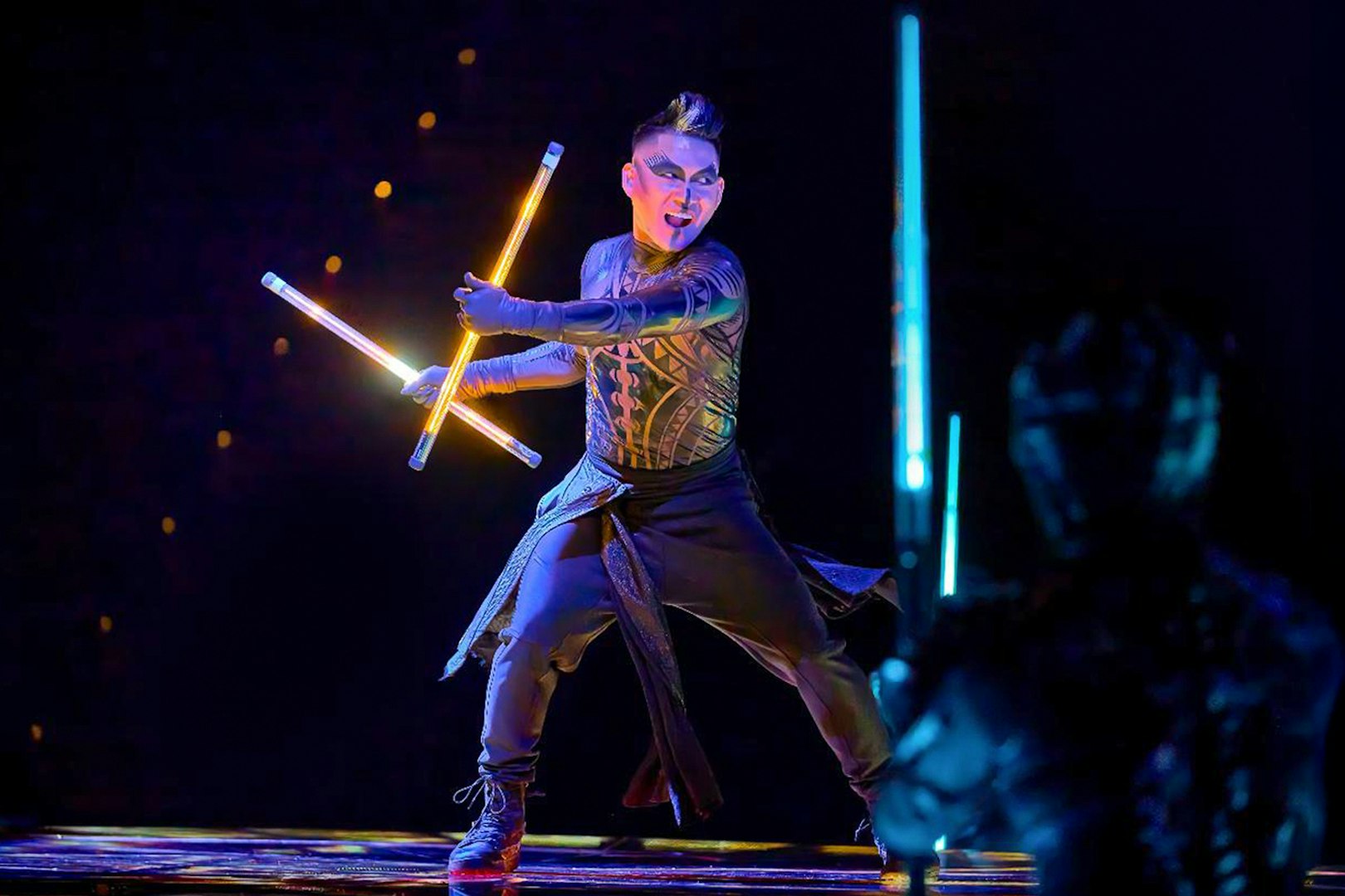 Performer with glowing batons on stage during Awakening show.