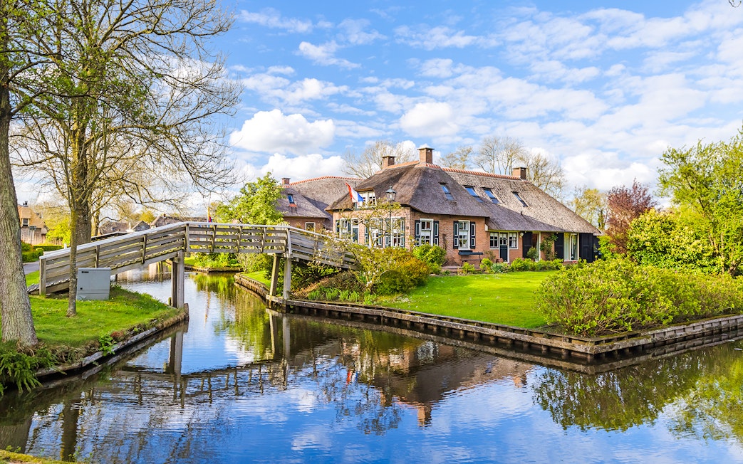 Thatched-roof house and wooden bridge over canal in Giethoorn, Netherlands.