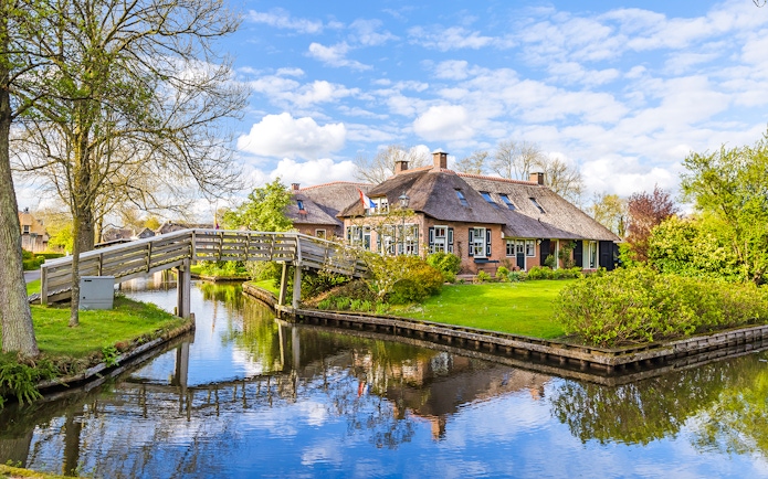 Thatched-roof house and wooden bridge over canal in Giethoorn, Netherlands.