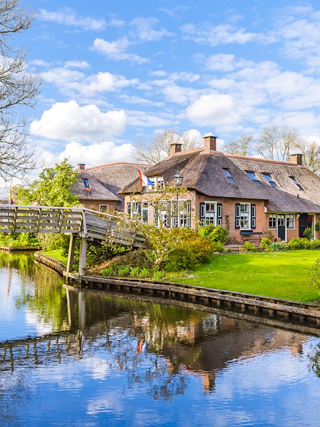 Thatched-roof house and wooden bridge over canal in Giethoorn, Netherlands.