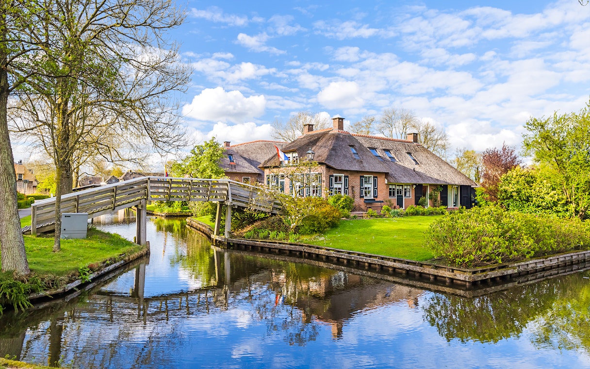 Thatched-roof house and wooden bridge over canal in Giethoorn, Netherlands.