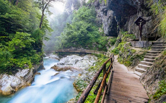 Wooden path and chapel at Vintgar Gorge, Slovenia, with flowing river and lush greenery.