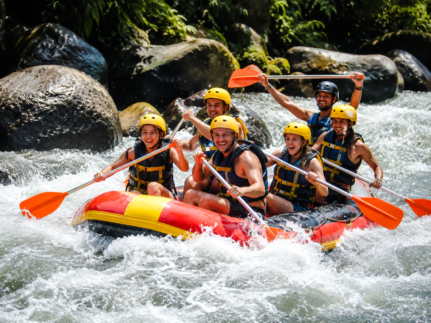 Group whitewater rafting on a river in Ubud, Bali, wearing helmets and life jackets.