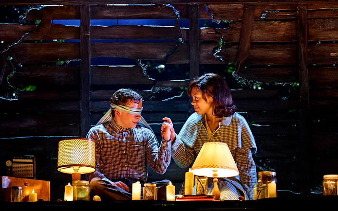 Two people in a dimly lit room with candles, one blindfolded, from "Stranger Things: The First Shadow.