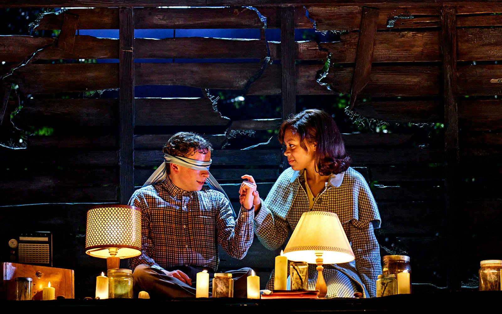 Two people in a dimly lit room with candles, one blindfolded, from "Stranger Things: The First Shadow.