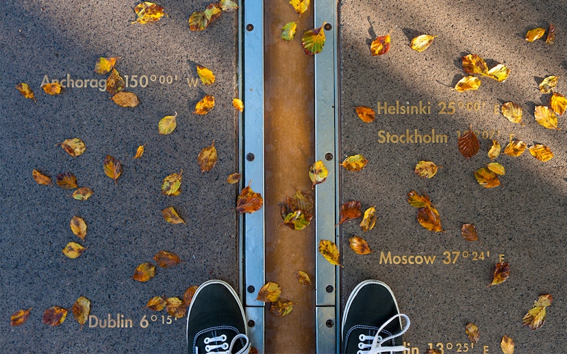 Prime Meridian line at Royal Observatory Greenwich with autumn leaves and city coordinates.