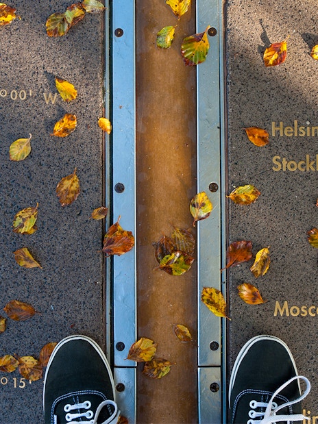 Prime Meridian line at Royal Observatory Greenwich with autumn leaves and city coordinates.