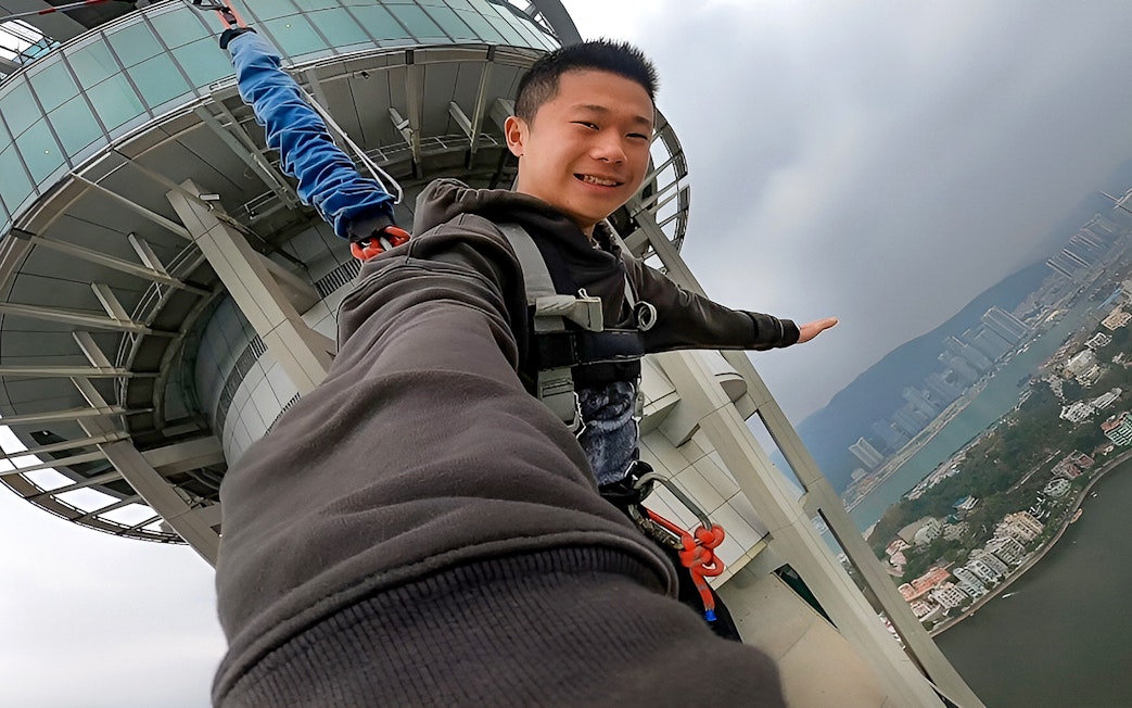 Person bungee jumping from Skypark Macau by AJ Hackett with city view.