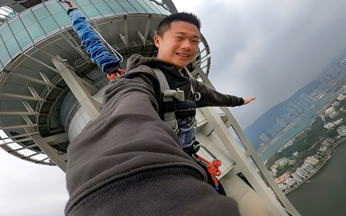 Person bungee jumping from Skypark Macau by AJ Hackett with city view.