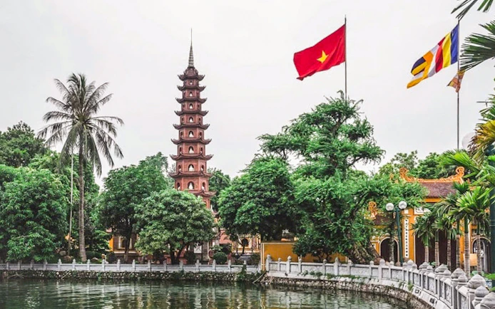 Tran Quoc Pagoda by the lake in Hanoi with Vietnamese flag.
