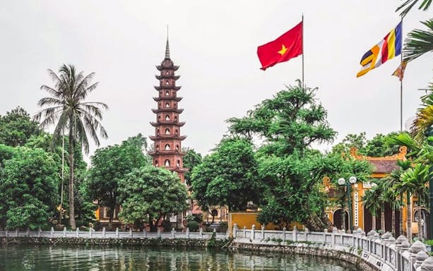 Tran Quoc Pagoda by the lake in Hanoi with Vietnamese flag.