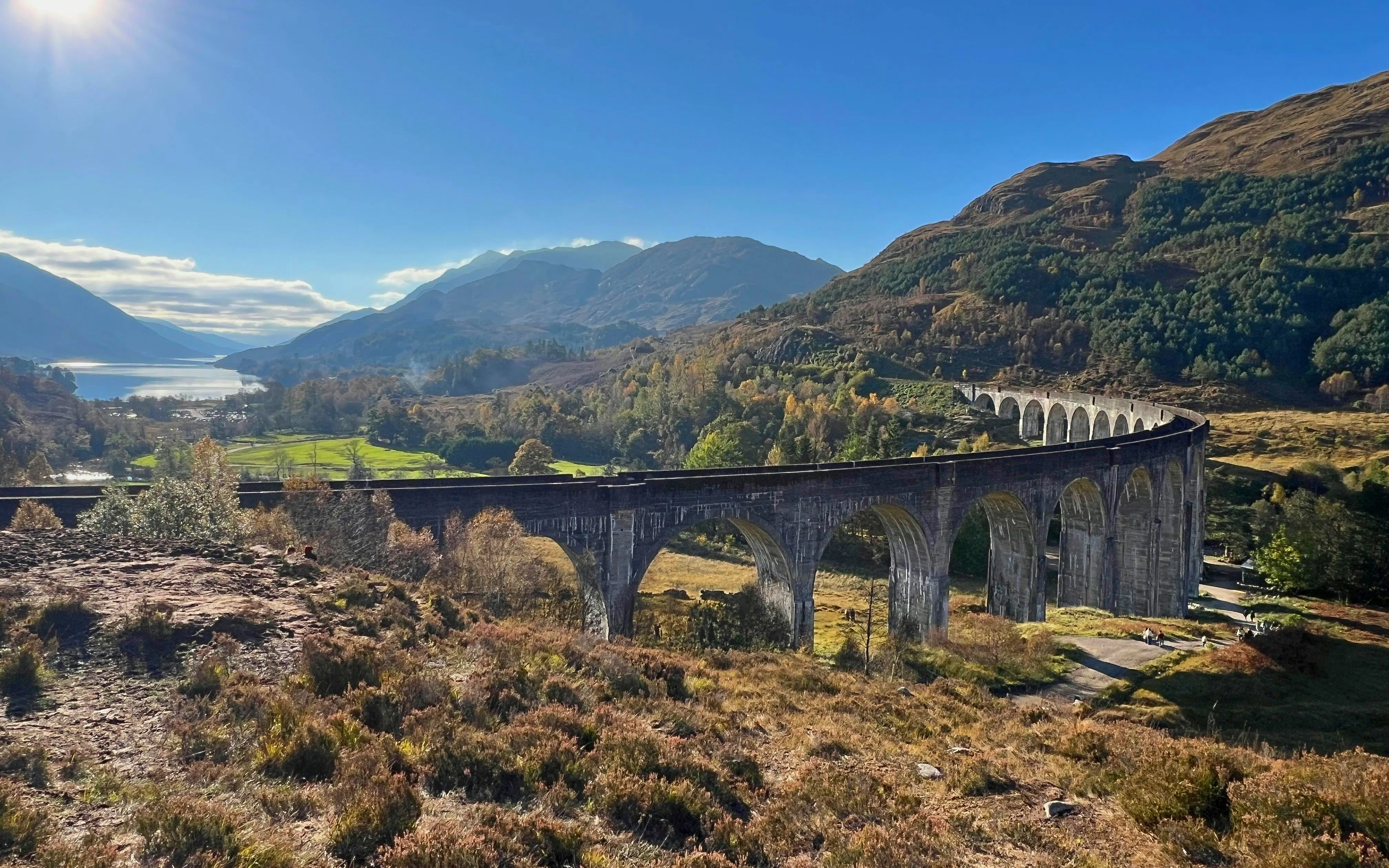 Glenfinnan Viaduct spanning lush Scottish Highlands with distant lake view.