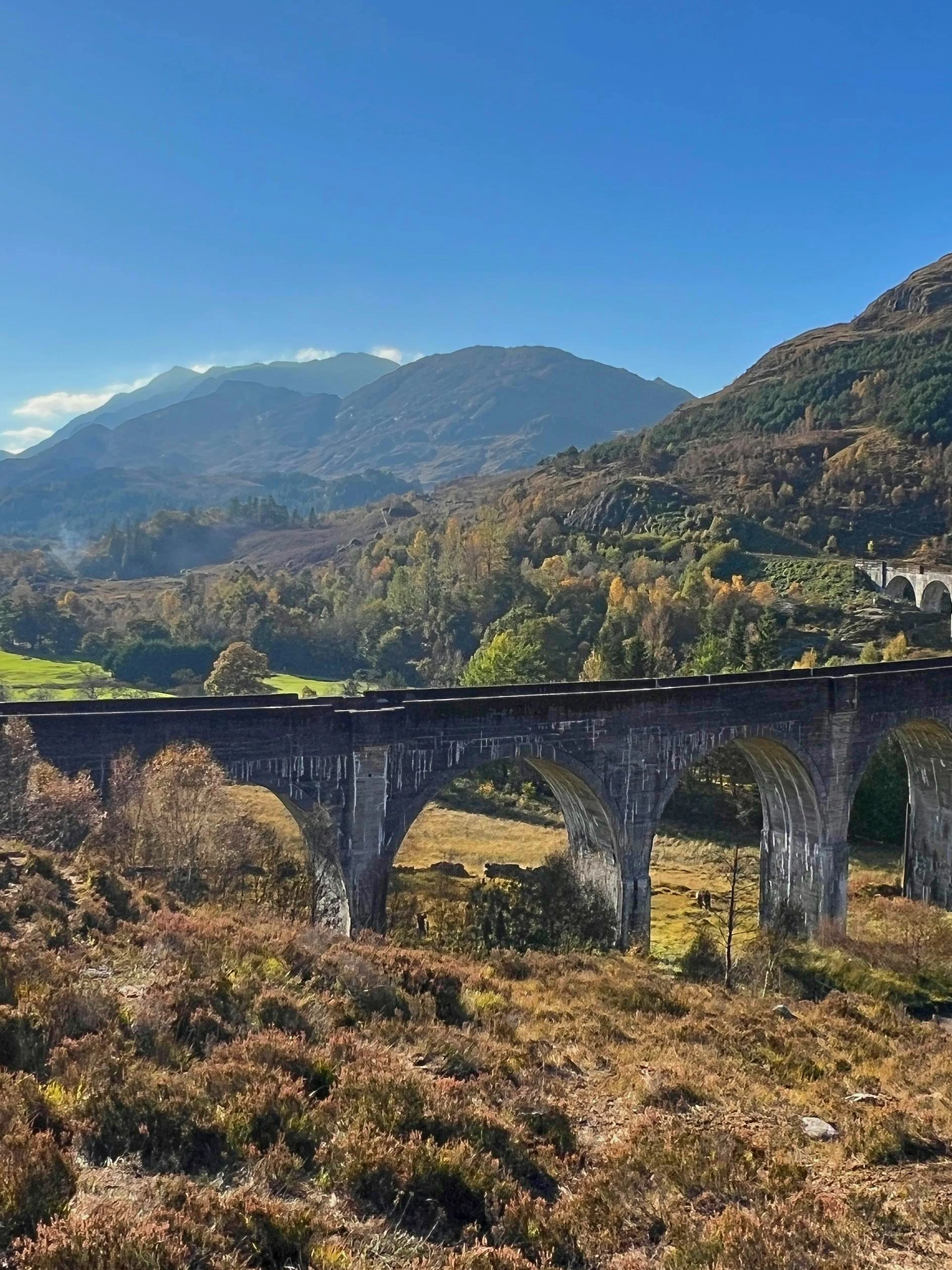 Glenfinnan Viaduct spanning lush Scottish Highlands with distant lake view.