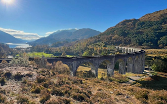 Glenfinnan Viaduct spanning lush Scottish Highlands with distant lake view.