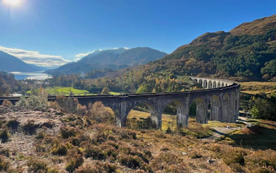 Glenfinnan Viaduct spanning lush Scottish Highlands with distant lake view.