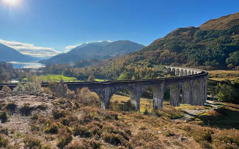 Glenfinnan Viaduct spanning lush Scottish Highlands with distant lake view.