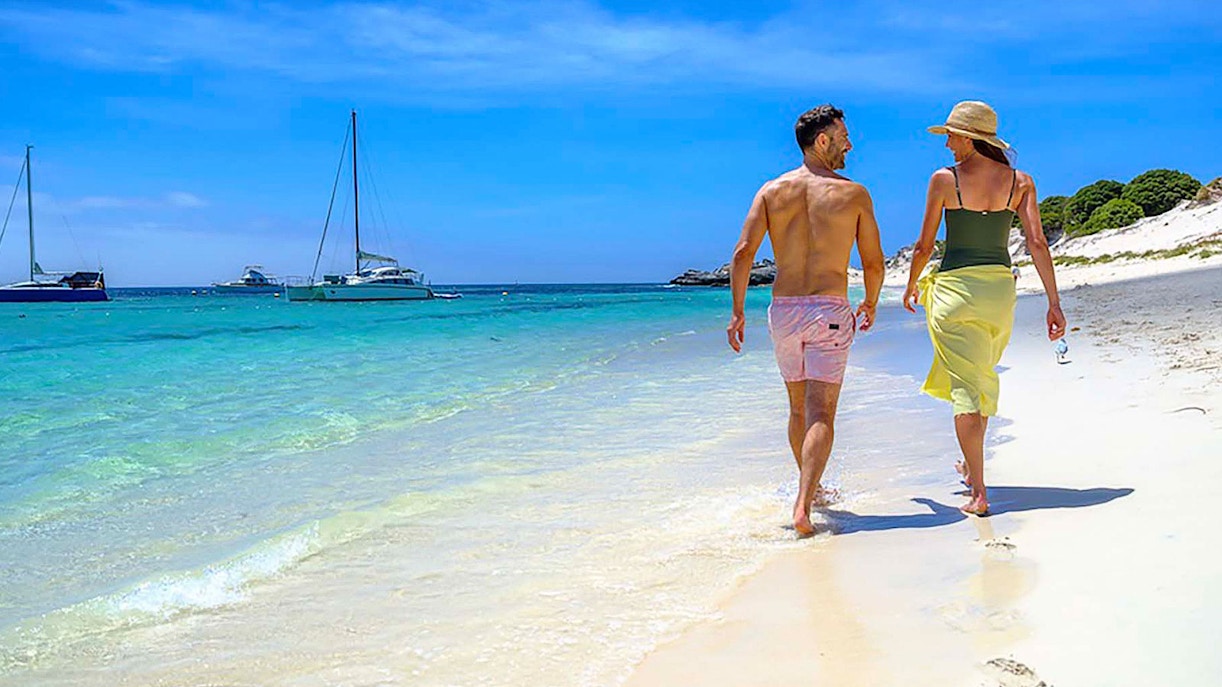 Couple walking along the beach with sailboats in the water at Rottnest Island.