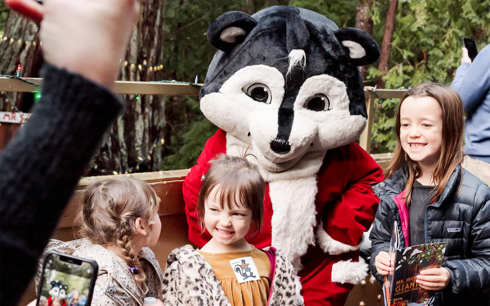 Kids smiling with Mr. Skunk mascot near the Giant Christmas Tree in Willits.