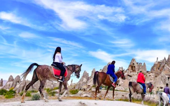 Guests horseback riding at sunrise in Cappadocia with rock formations in the background.