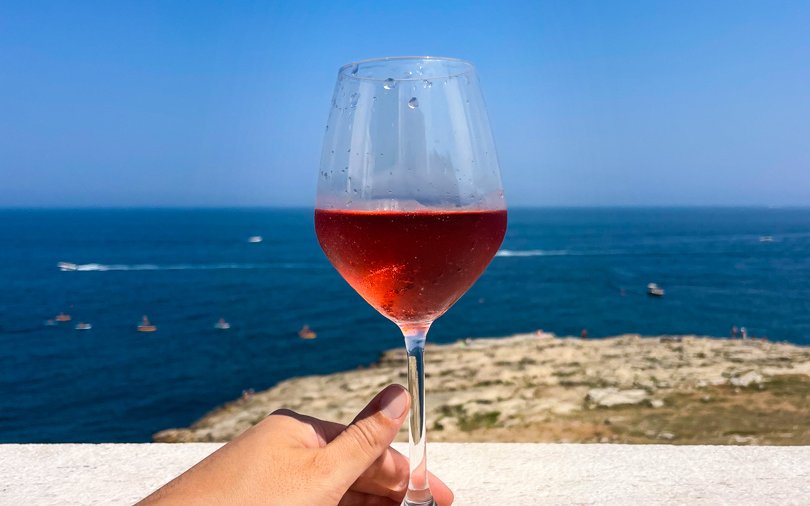 Wine glass held against the sea view in Polignano a Mare during street food tour.