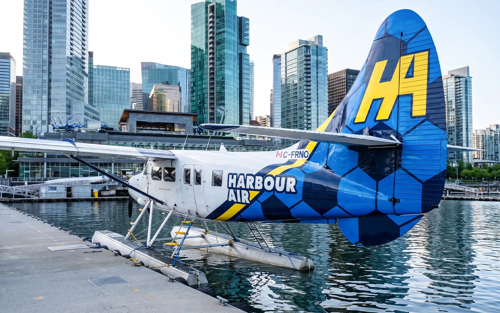 Seaplane docked in Vancouver harbor with city skyline in background.