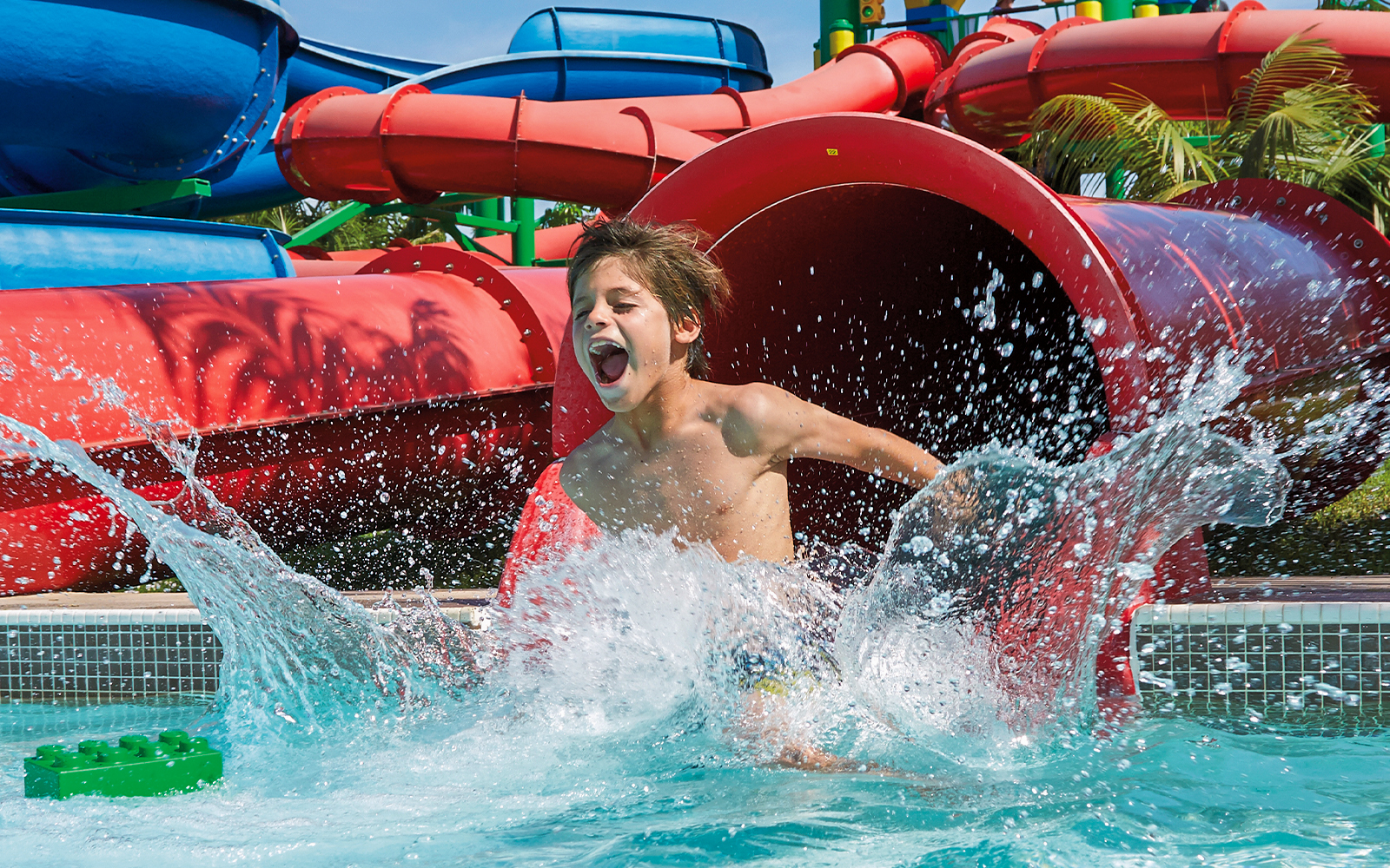 Kid splashing in pool at Dubai water park with colorful slides.
