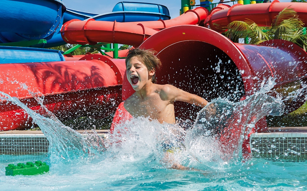 Kid splashing in pool at Dubai water park with colorful slides.