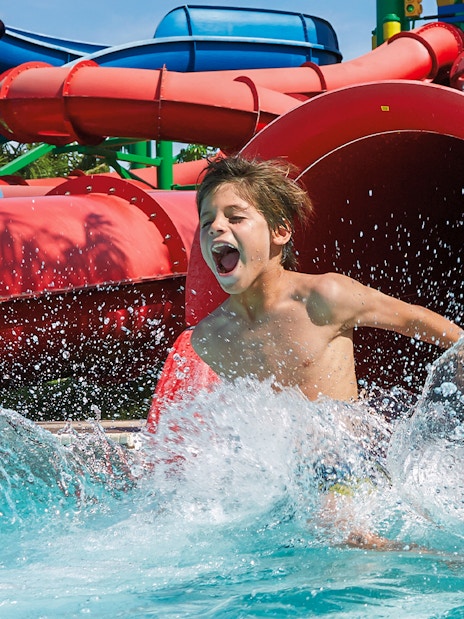 Kid splashing in pool at Dubai water park with colorful slides.