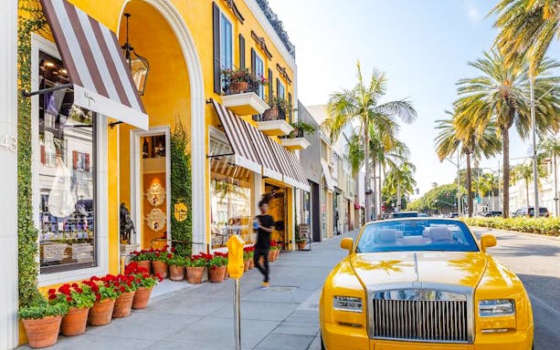 Yellow luxury car parked on Rodeo Drive, Beverly Hills, with palm trees and upscale shops.